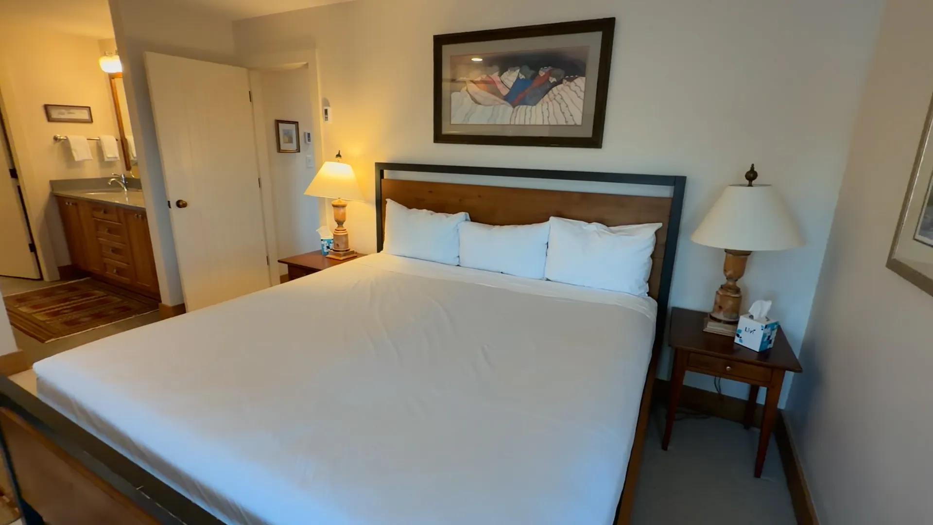 Master bedroom king bed with mountain artwork above headboard and ensuite bathroom doorway - Spring Creek Ranch Jackson Hole